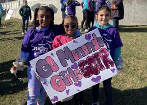 Group shot of Girls on the Run members holding a sign cheering on other runners