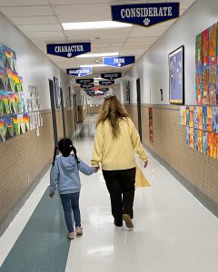 Student holds the hand of a staff member while walking in an empty hallway