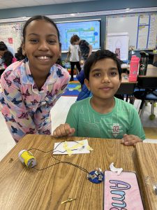 Two students smile while posing in front of an experiment