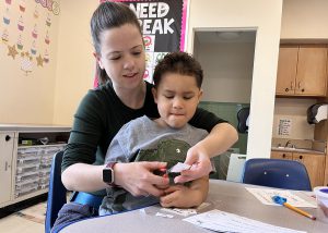 An aide helps a student cut paper