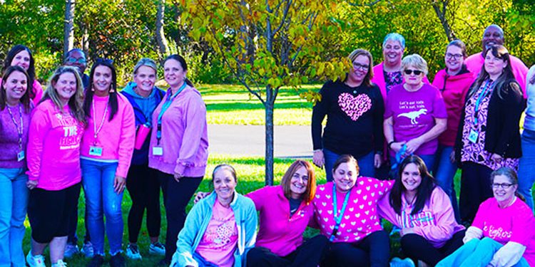 Teachers wearing pink pose around a tree