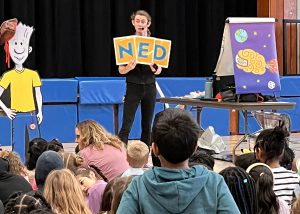 Presenter standing in front from a crowd holding a NED sign