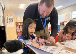 A police officer helps a student as the student points to something on a handout