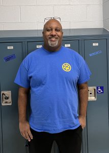 Taj Buskey smiles while posing in a blue tee shirt